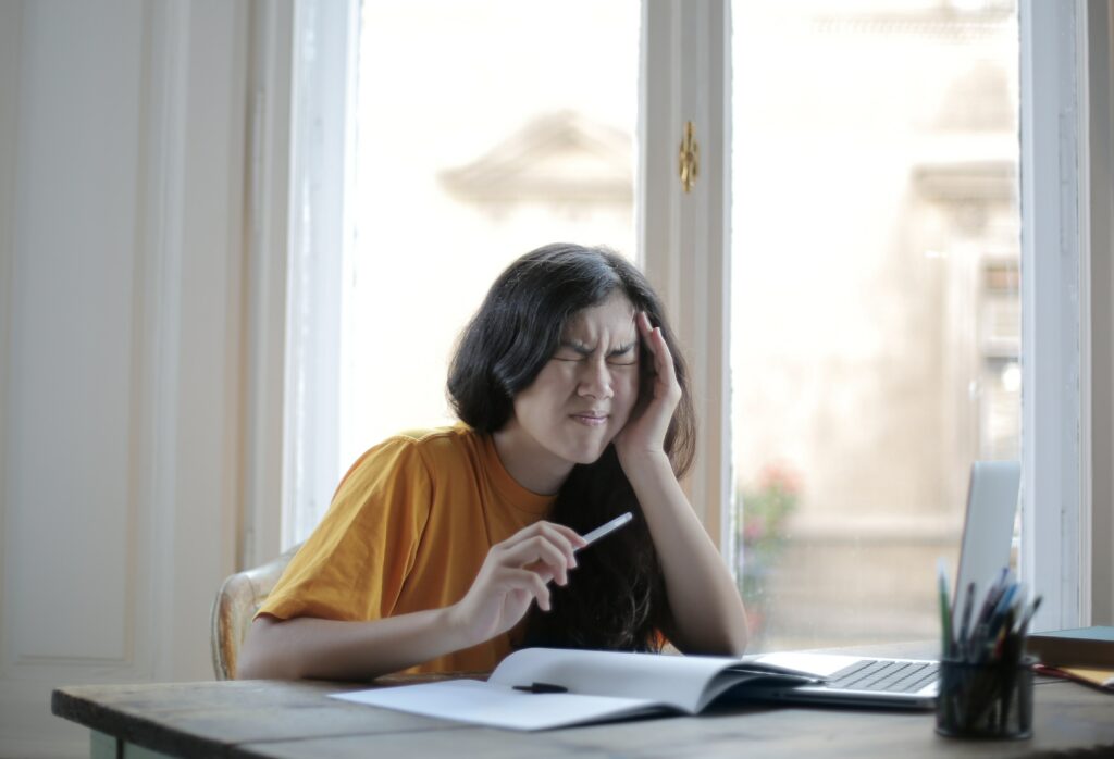 Woman sitting at a table holding her head stressed while working.