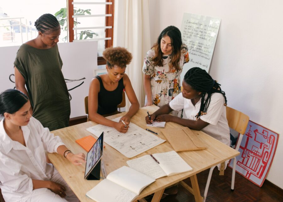 A group of five women work around a table designing a product.