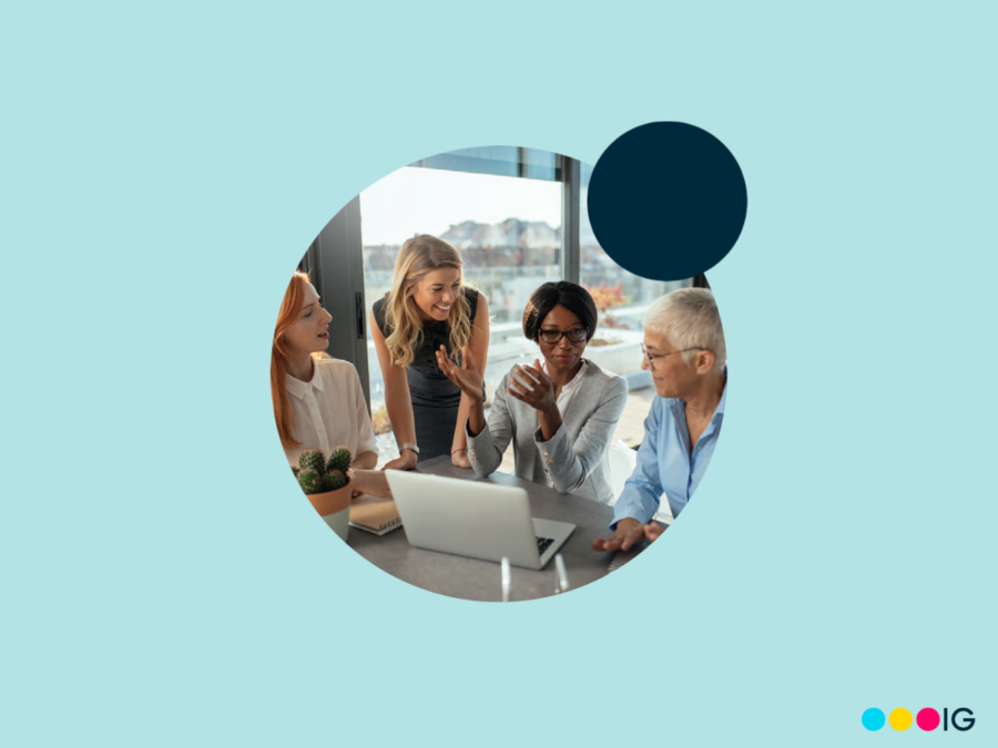 Circle crop photo of four women smiling and working around a computer. Navy blue accent circle. Light blue background.