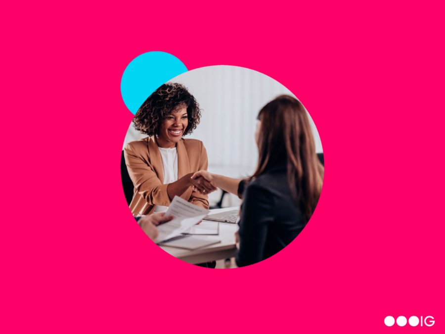 Photo of two women shaking hands at a job interview surrounded by a pink background with What Is A Marketing Director Job Description, Salary, and More